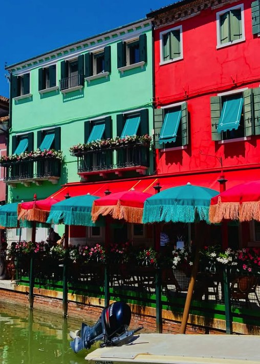 Fringed parasols over a canal-side restaurant beneath bright green and red Burano houses