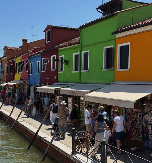 Visitors walking Burano's fondamenta past souvenir and lace stalls under white awnings