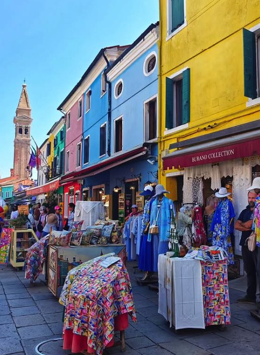 Lace and linen stalls on Burano's main street with the leaning campanile of San Martino behind