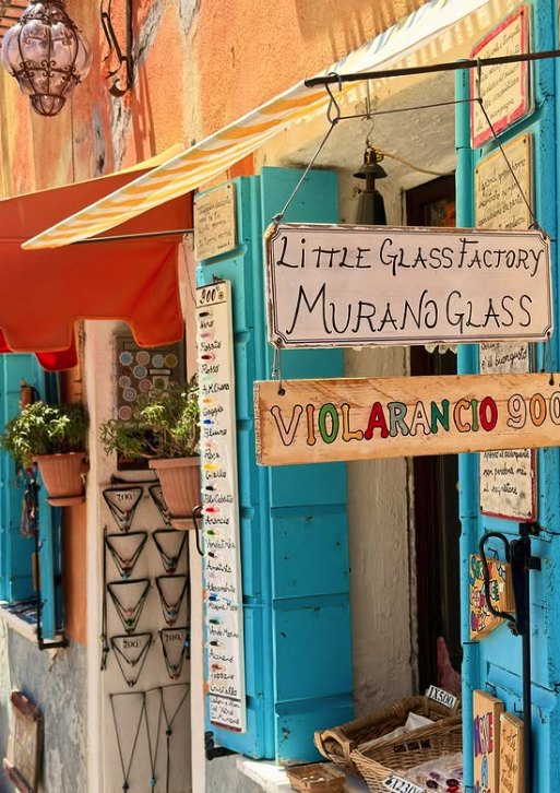 A hand-painted Little Glass Factory sign outside a Murano glass shop hung with bead necklaces
