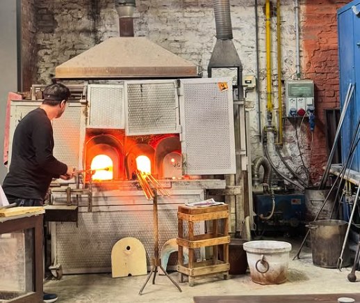 A glassmaker working at the open mouth of a furnace inside a Murano glassworks