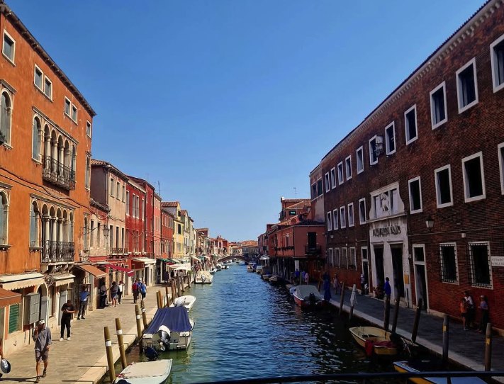 Murano's Canal Grande with brick palazzi on both banks and small boats moored along the fondamenta