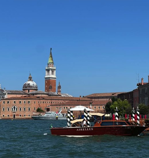 A varnished wooden water taxi crossing the lagoon in front of the campanile of San Giorgio Maggiore